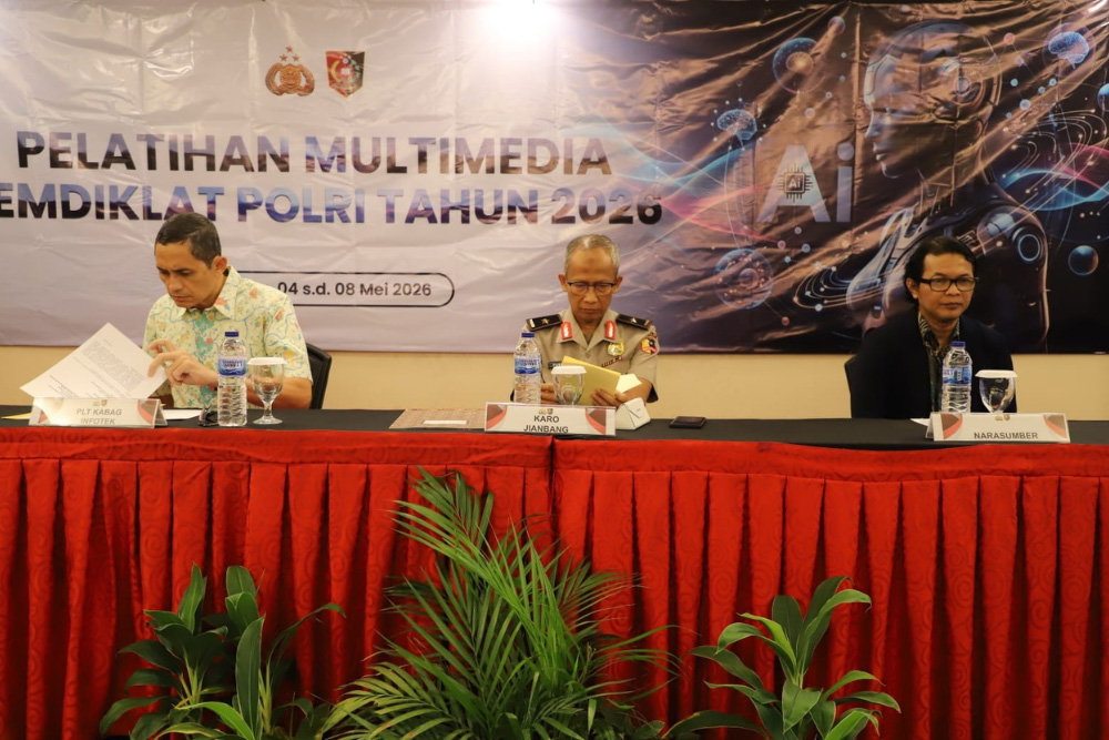 Three men sit at a long table with a red skirt, reading and speaking during a conference, with a science/tech banner in the background.