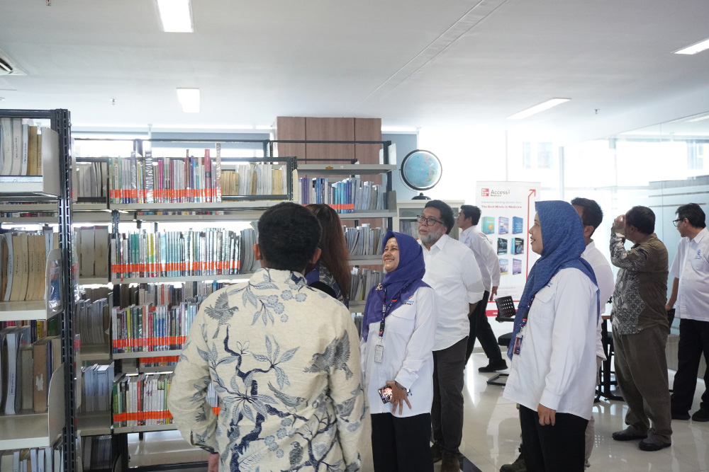 Group of professionals touring a library, browsing tall shelves of books.