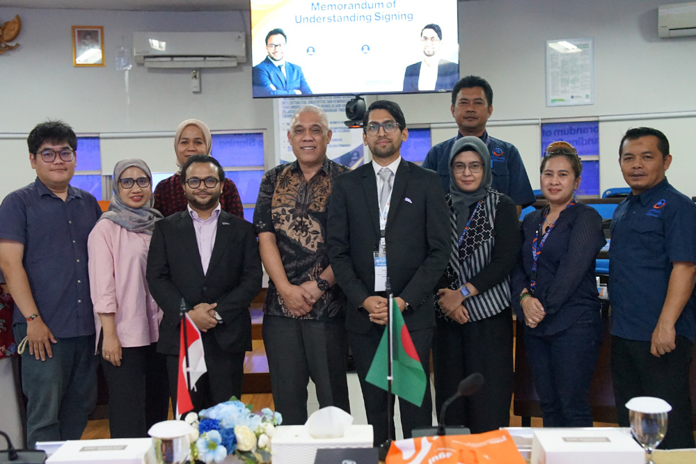 Group photo at a Memorandum of Understanding signing event with diverse professionals and two flags on the table in front of them.