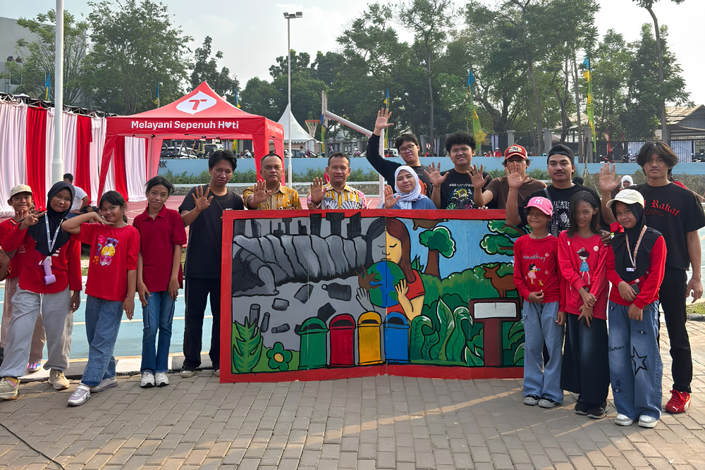 Group of adults and children posing behind a colorful mural at an outdoor community event in the afternoon.